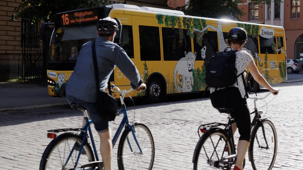 Kaksi pyöräilijää kaupungissa, taustalla linja-auto